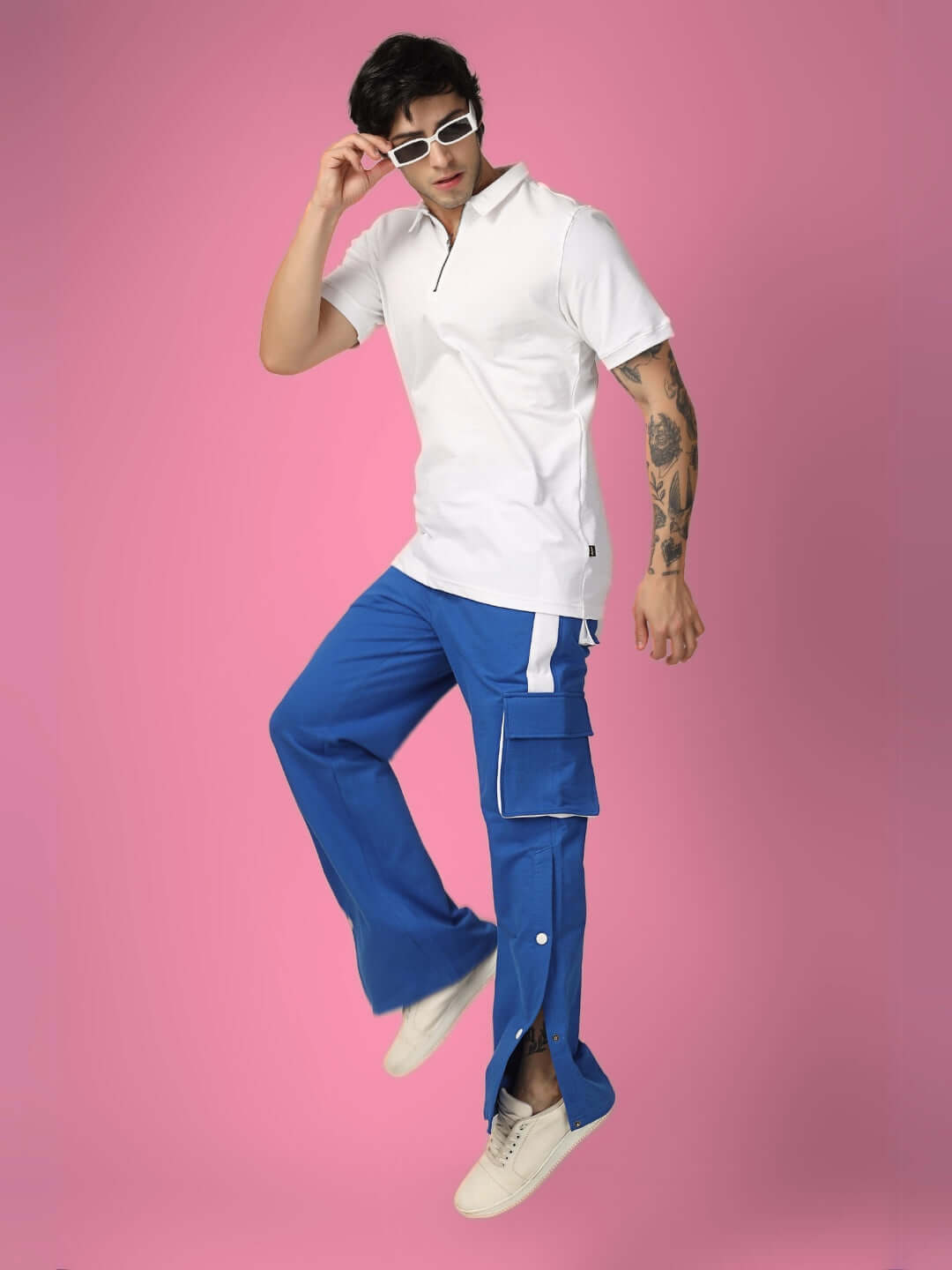 Model wearing BRACKET cargo pant in blue with white highlights, posing against pink background, featuring custom fit option.