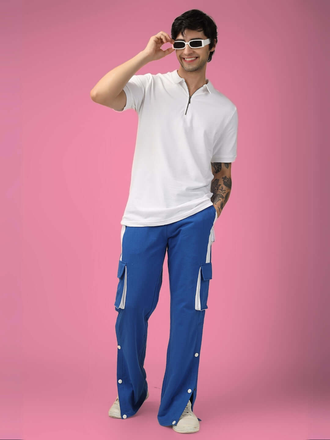 Model wearing blue and white highlighter bracket cargo pants, paired with a white polo shirt, standing against a pink background.