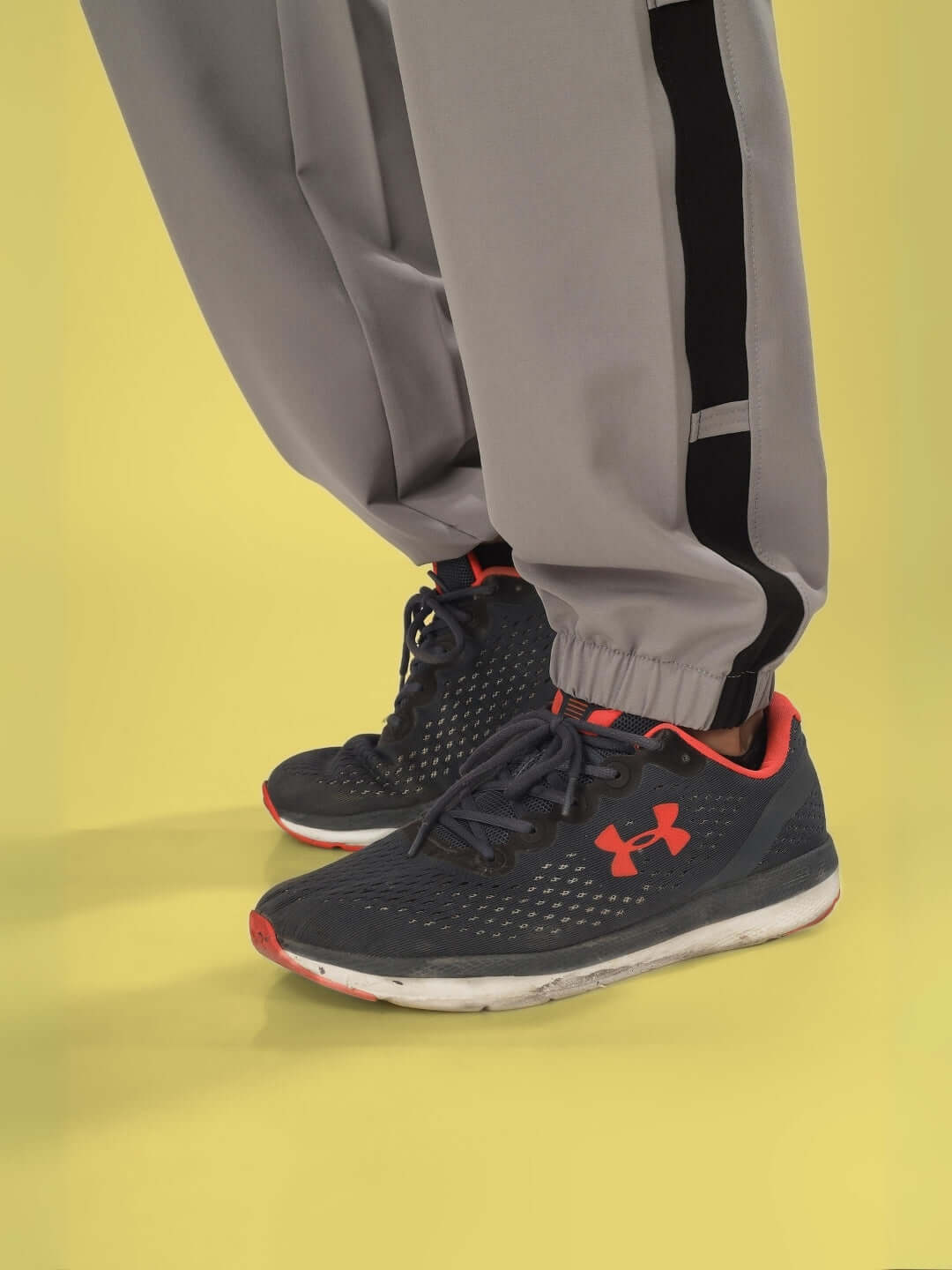 Close-up of BRAVO Relaxed Fit Cargo Pants in grey, showcasing customizable fit option, paired with navy sneakers on yellow background.
