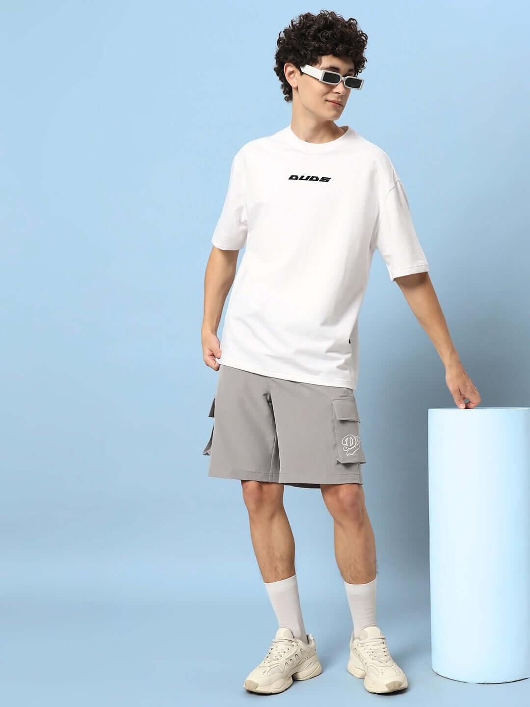 Model wearing Brawny Cargo Shorts in grey, styled with a white t-shirt and sneakers, showcasing customizable casual wear.