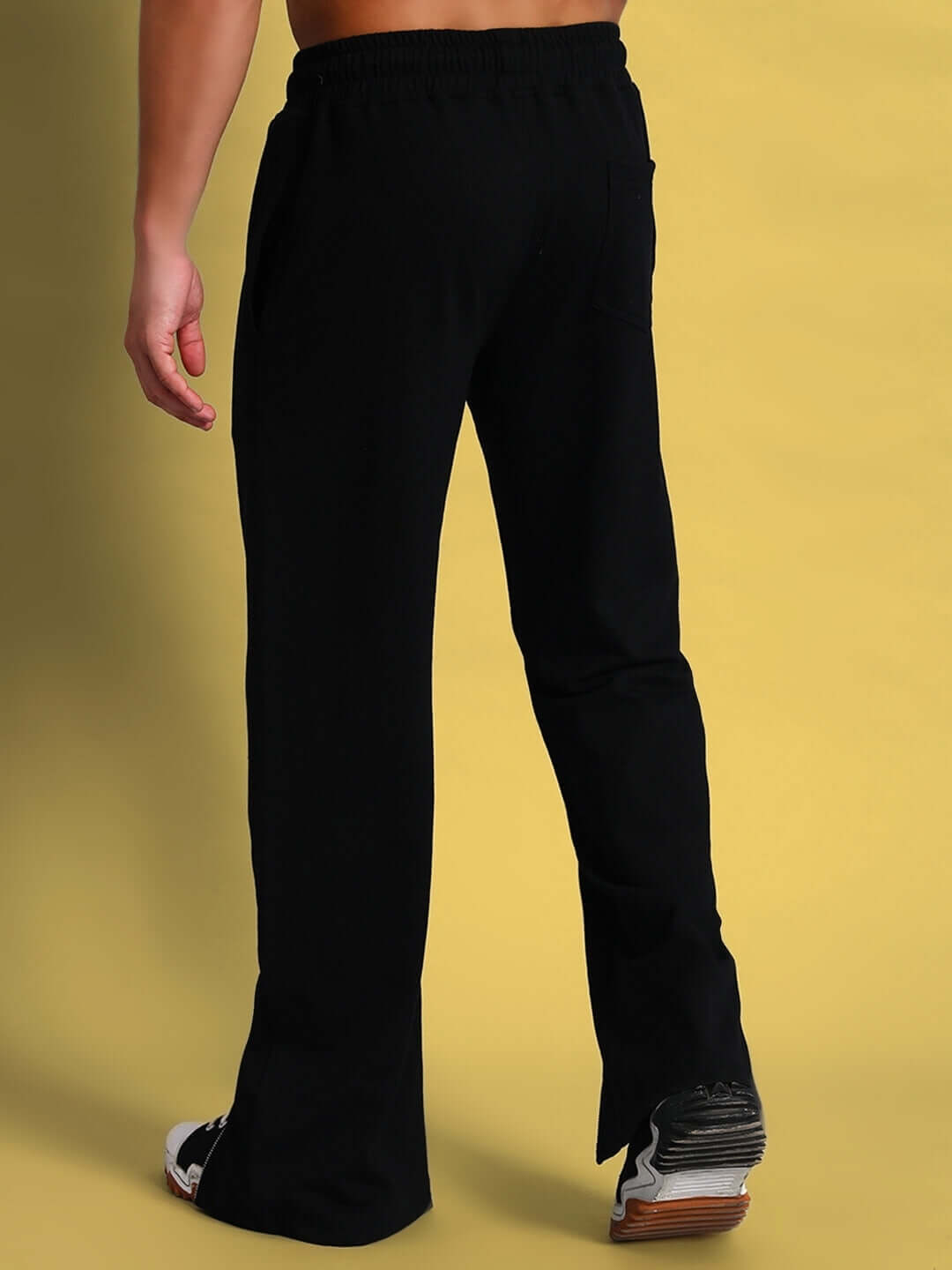 Model wearing black open zipper joggers from DUDS, showcasing rear view and fit against a yellow background.