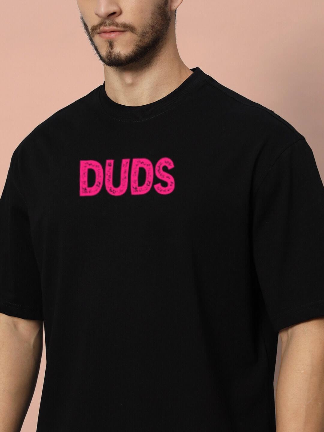 Man wearing BREAKING OVER-SIZED T-SHIRT BLACK with pink 'DUDS' text, showcasing streetwear style and relaxed fit.