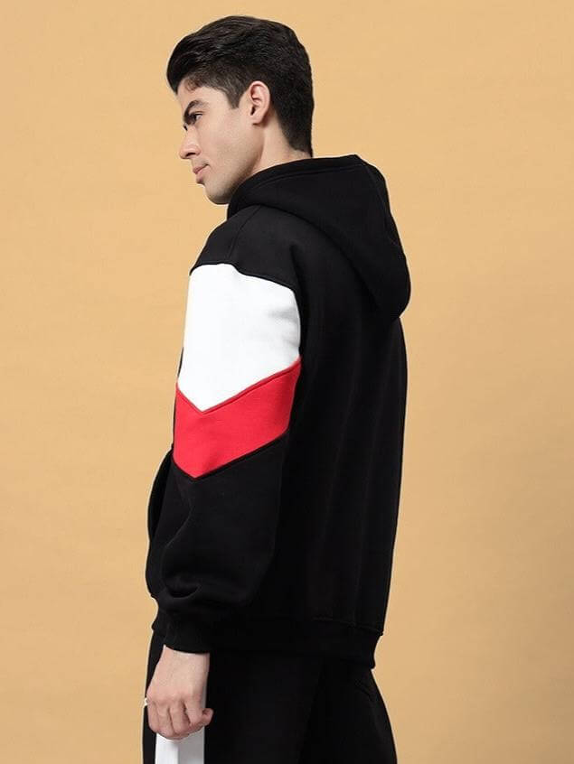 Side view of a model wearing the BRIO FLEECE COLORBLOCK HOODIE BLACK with red and white details on sleeves.