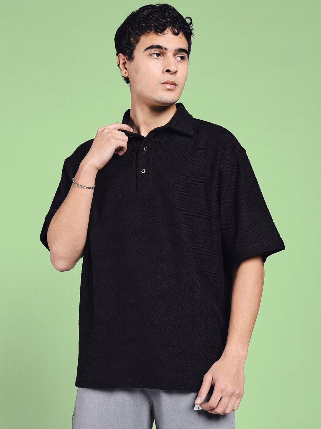 Model wearing BROCADE POLO COTTON T-SHIRT BLACK in intricate cotton jacquard, showing style and comfort on a green background.