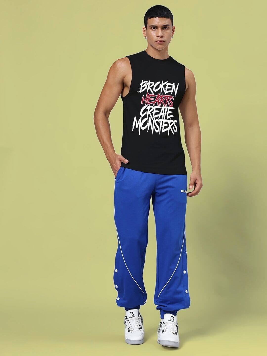 Model wearing BROKEN HEART PRINT SLEEVELESS T-SHIRT BLACK with blue pants and sneakers, showcasing bold graphic design and street style.