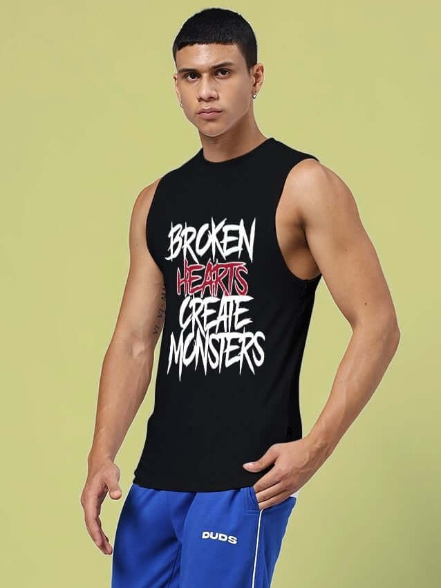 Man wearing BROKEN HEART PRINT SLEEVELESS T-SHIRT BLACK with unique design and graphic text on front, casual and trendy style.