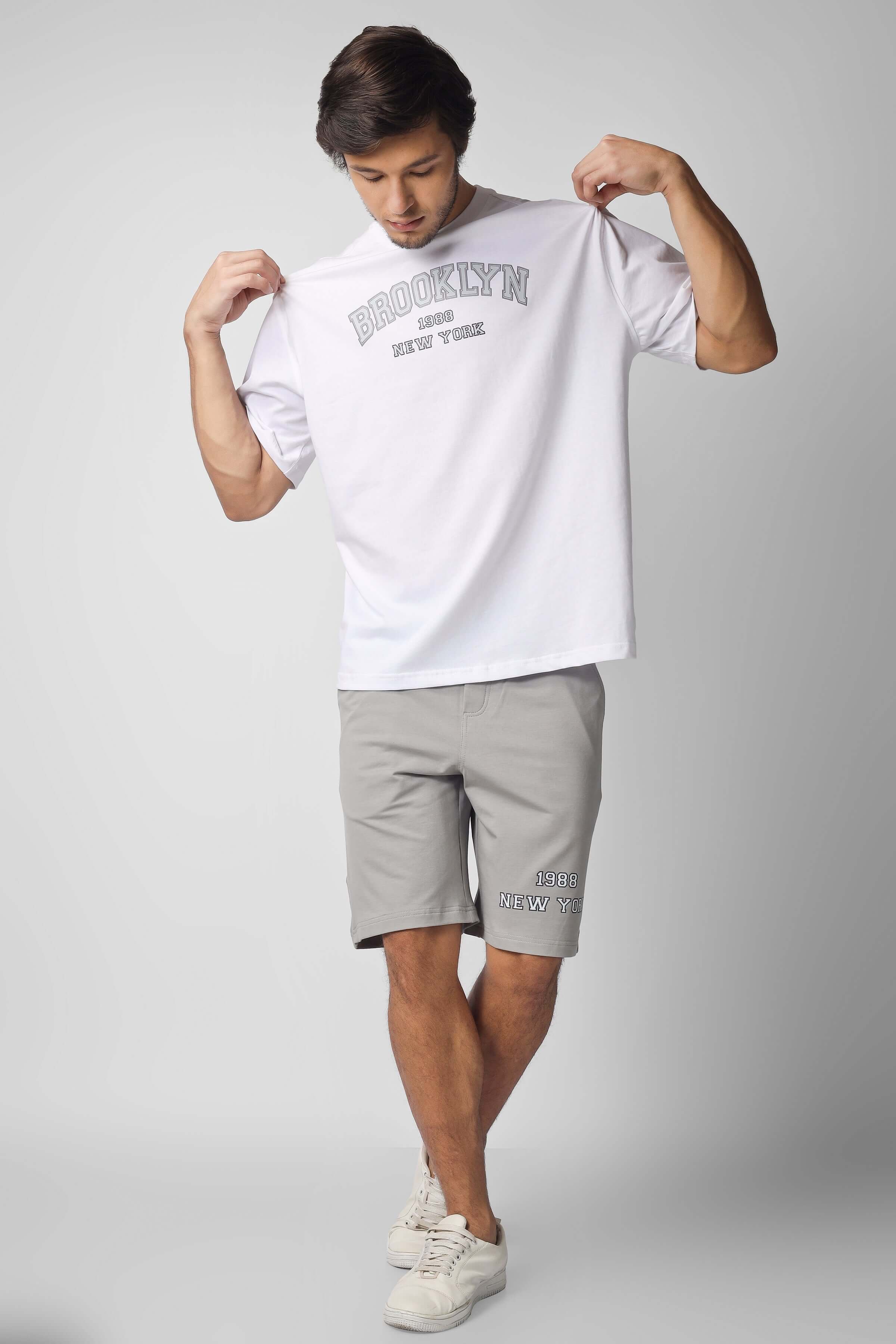 Man modeling Brooklyn Co-ord Set in white and grey, featuring a casual t-shirt and shorts, highlighting custom fit options.