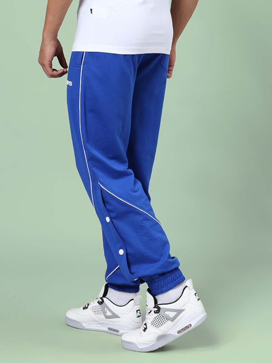 A side view of BROSSFINE CONTRAST JOGGERS ROYAL BLUE with sleek contrast detailing, worn with white sneakers.