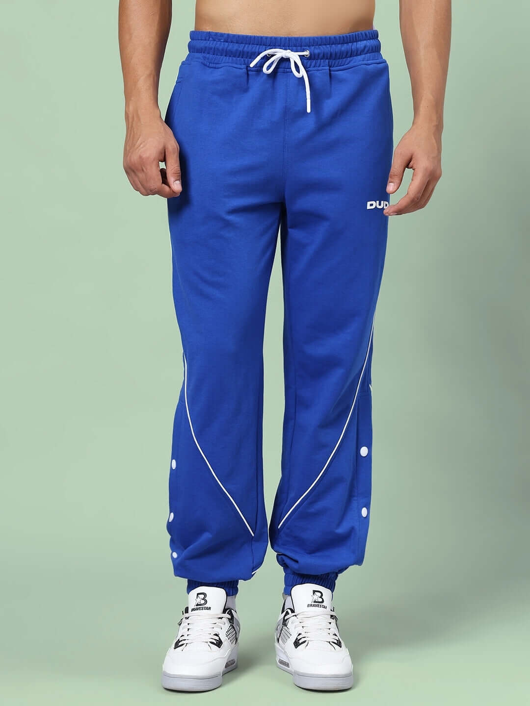 Man wearing BROSSFINE CONTRAST JOGGERS ROYAL BLUE with white shoes against green background.