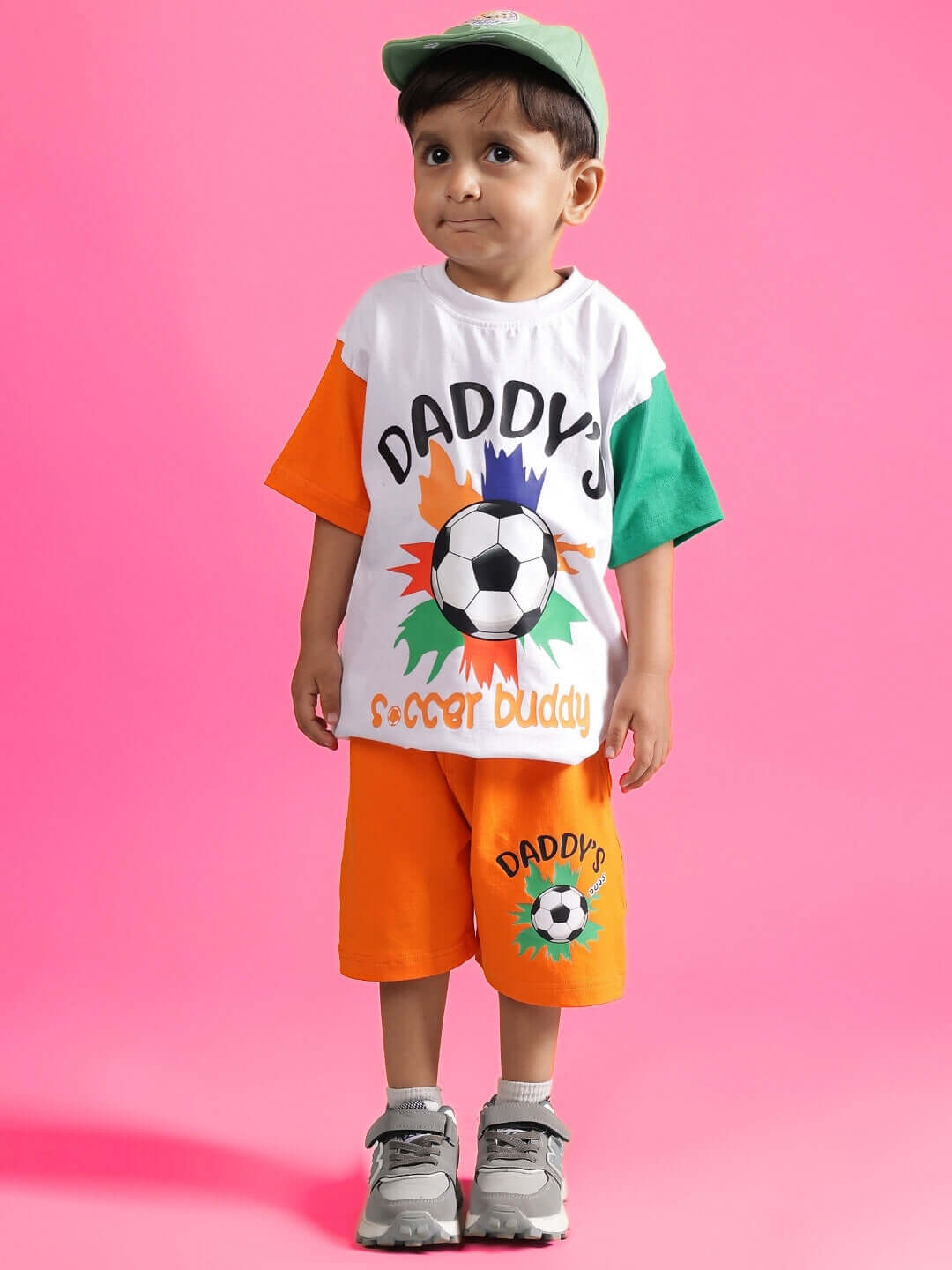 Child wearing BUDDY CO-ORD FOR BOYS & GIRLS WHITE-ORANGE, with a soccer-themed design on a pink background.
