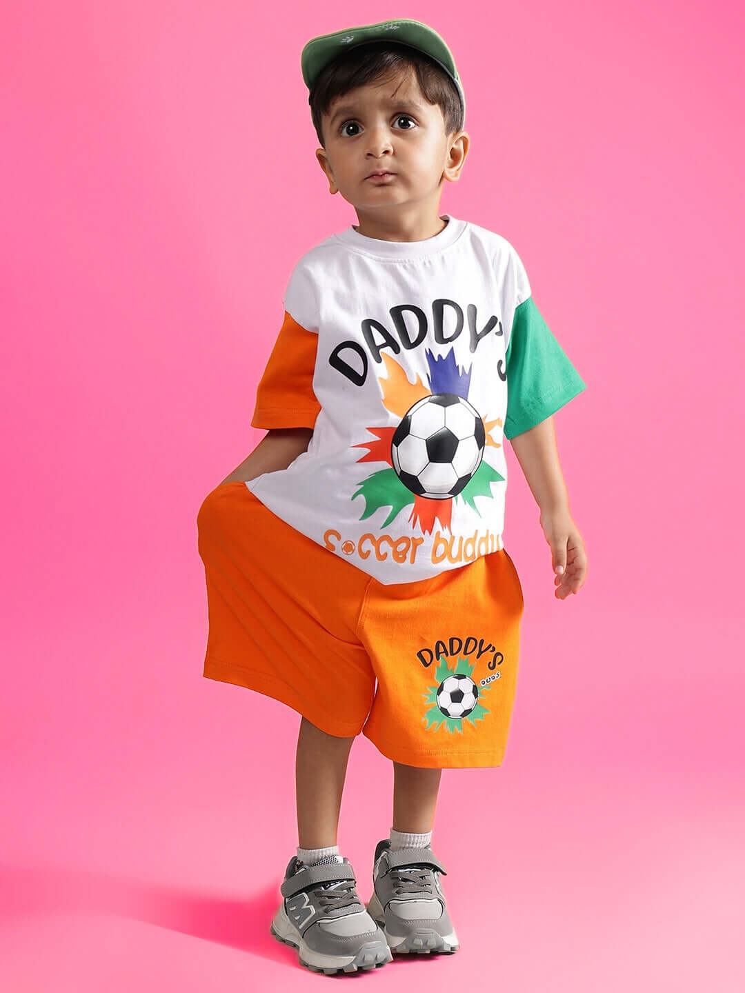 Child wearing the BUDDY CO-ORD FOR BOYS & GIRLS WHITE-ORANGE outfit featuring a soccer theme against a pink background.