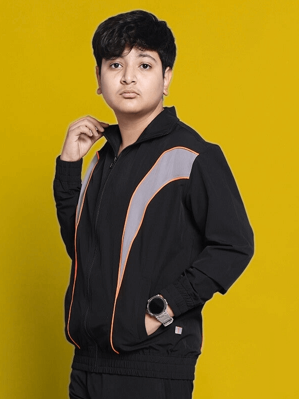 Child wearing black Bullet Parachute Jacket by DUDS with contrast stripes, posing on a yellow background.