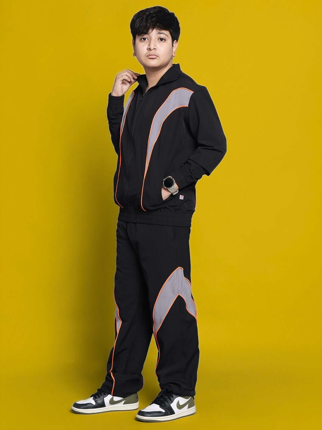 Child wearing black bullet parachute jacket with orange accents, styled for boys and girls, standing confidently against a yellow background.