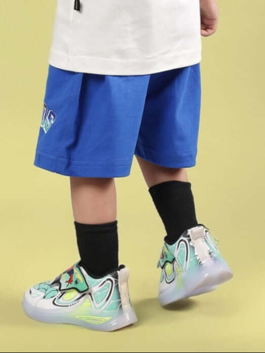 Child wearing BUMBLE SHORTS FOR BOYS & GIRLS ROYAL BLUE with colorful sneakers, showcasing comfortable fit and vibrant style on a yellow background.