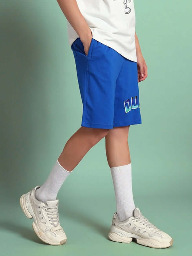 Boy wearing blue Bunny Bugs summer shorts with white socks and sneakers, featuring DUDS logo on shorts.