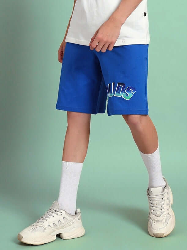 Model wearing blue Bunny Bugs summer shorts by DUDS, showcasing casual style with white sneakers and socks.