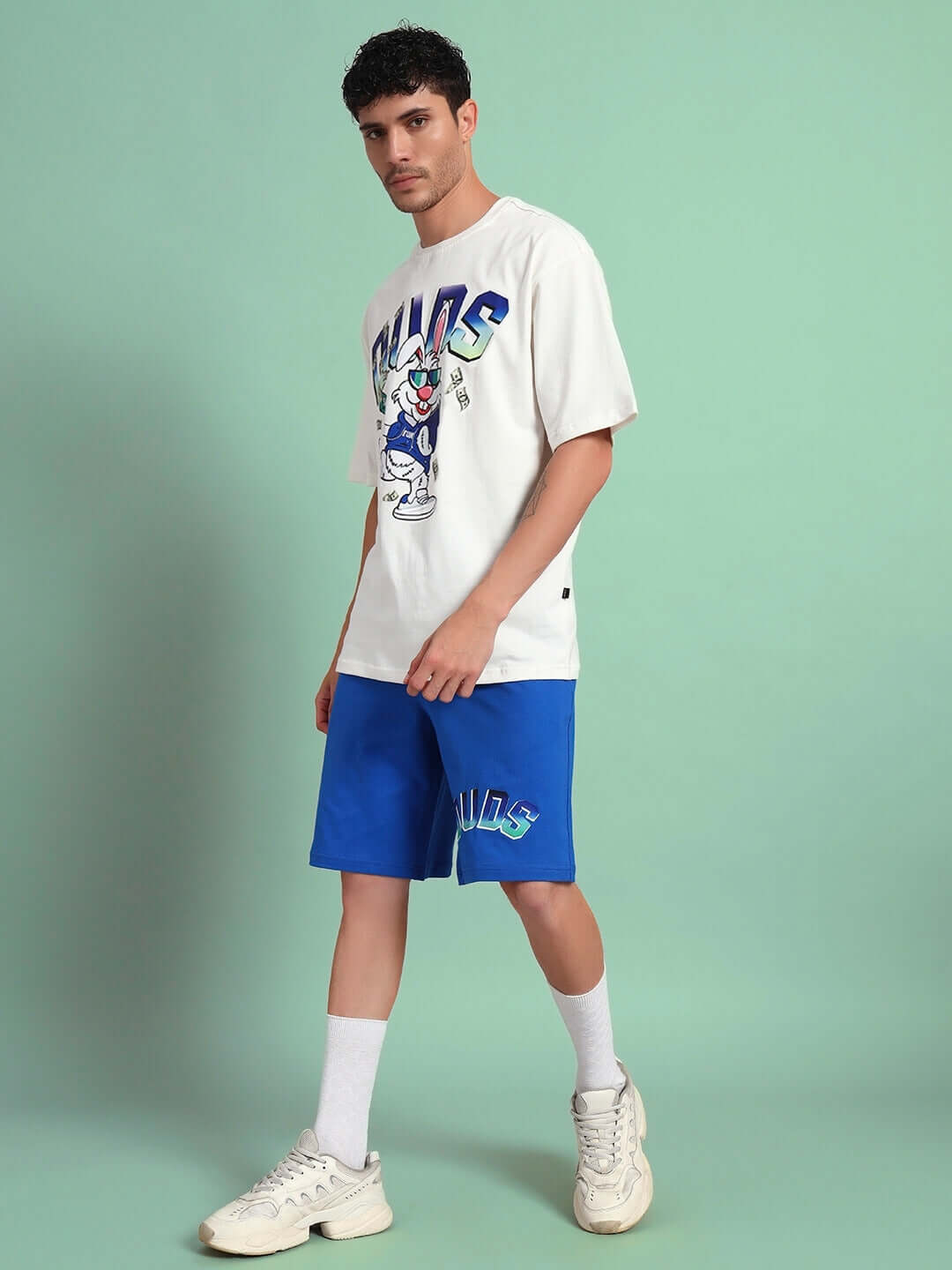 Man wearing BUNNY BUGS CO-ORD SET OFF-WHITE BLUE with cartoon print, featuring premium cotton fabric, styled against a green background.