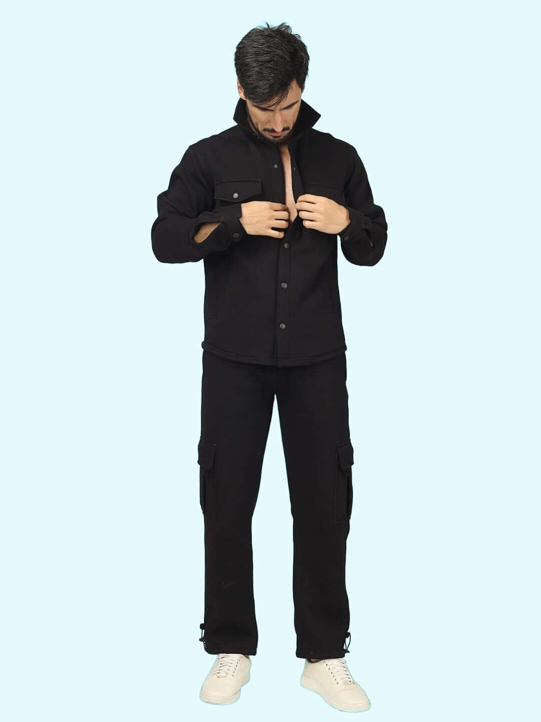 Man wearing a black overshirt and cargo pants set, adjusting collar.