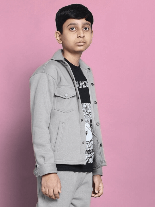 Boy wearing a grey fleece sweatshirt, standing against a pink background.
