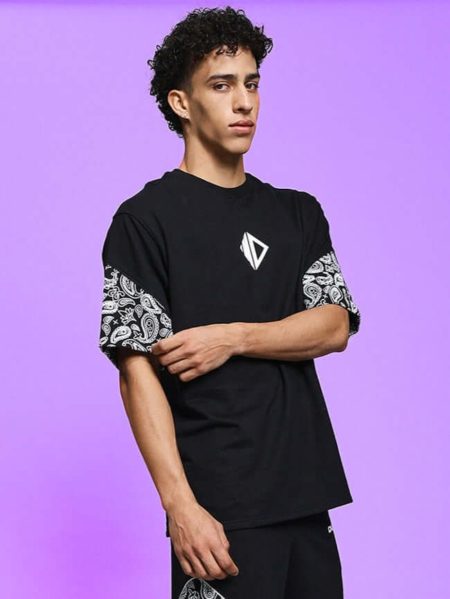Model wearing CALVIN OVER-SIZED T-SHIRT BLACK, showcasing relaxed fit and stylish design against a purple background.