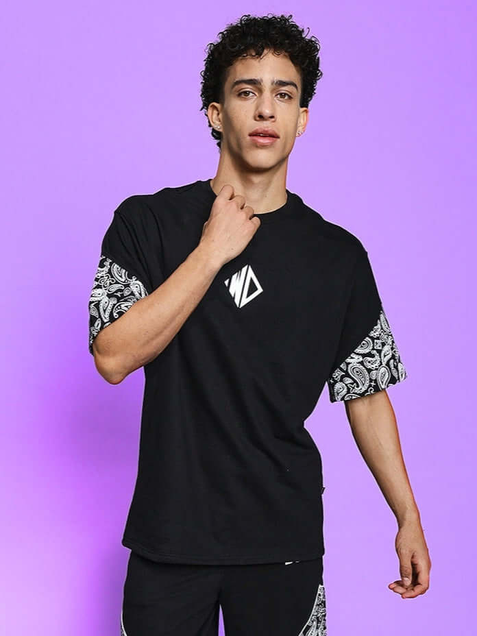 Model wearing CALVIN OVER-SIZED T-SHIRT BLACK with printed sleeves against a purple background.