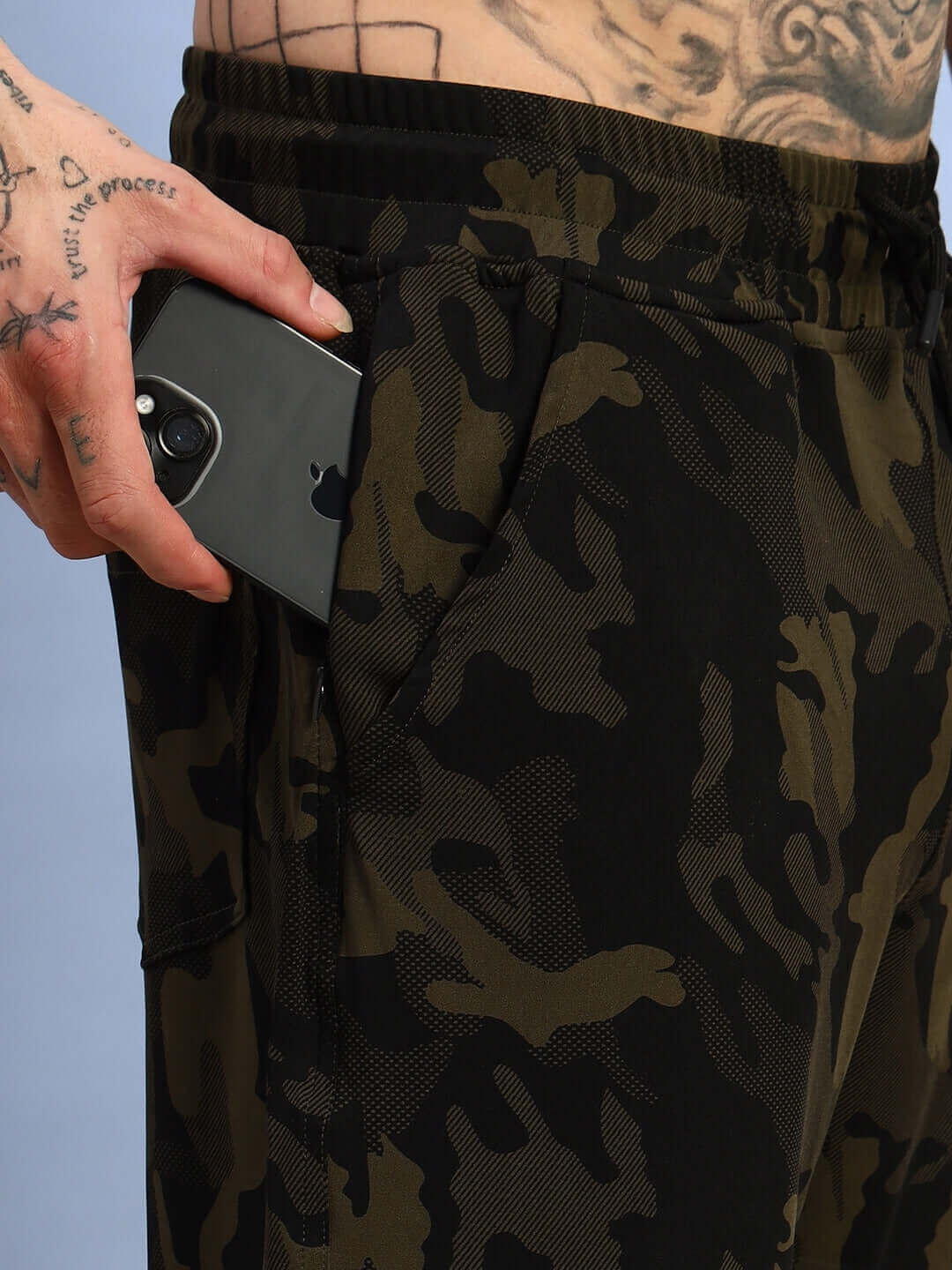 Person wearing camo green trench relaxed pant jogger with a phone in pocket.