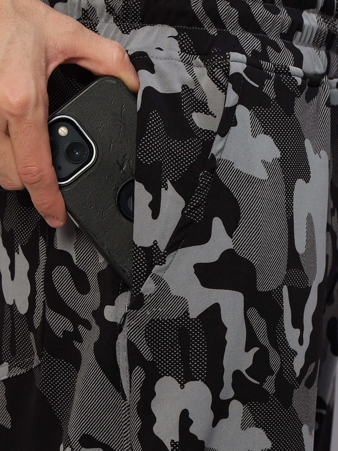 Close-up of a hand placing a smartphone in the pocket of navy camo relaxed jogger pants by DUDS.