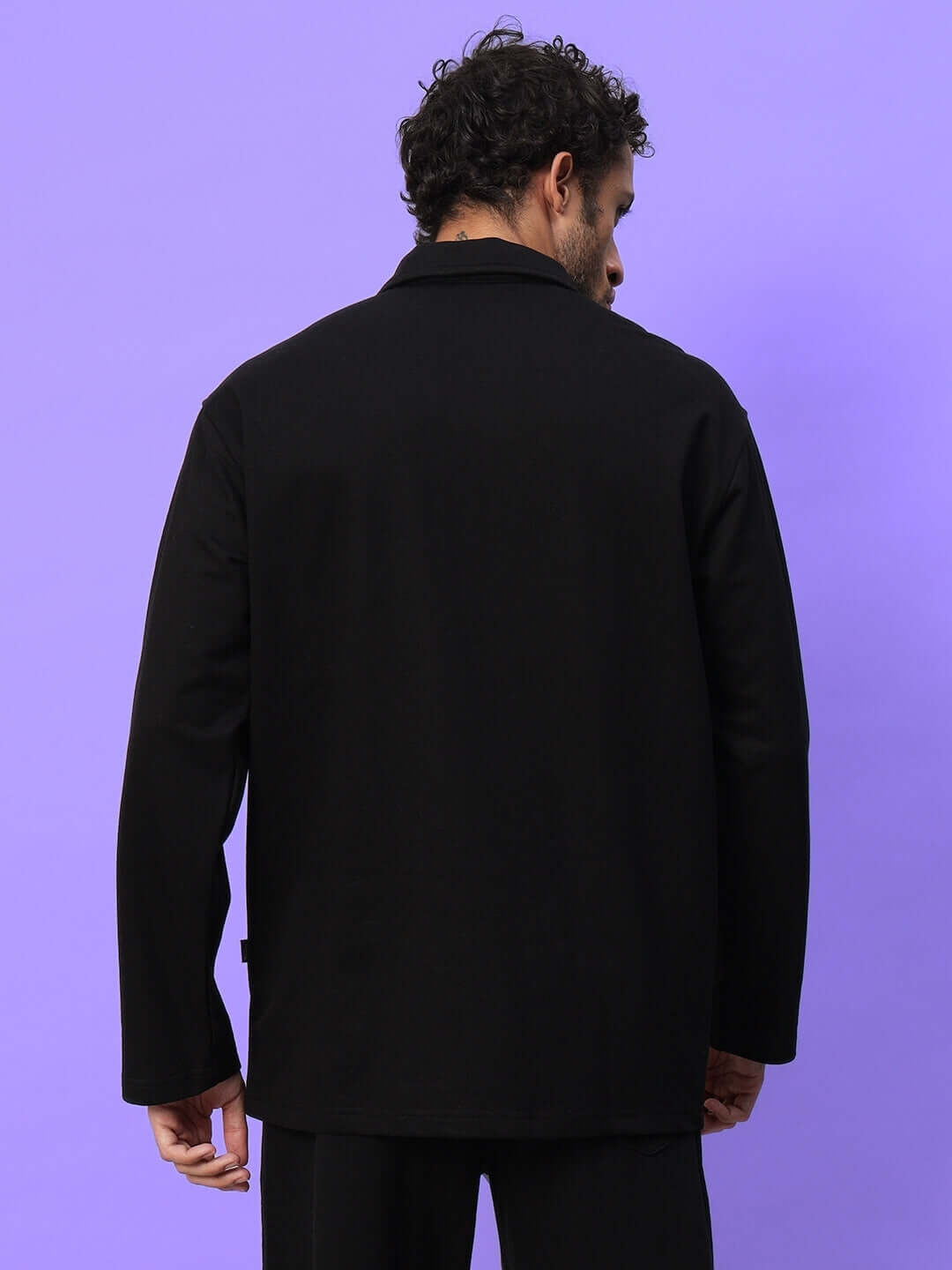 Back view of a man wearing a black oversized sweatshirt, showcasing its relaxed fit and casual style against a purple background.