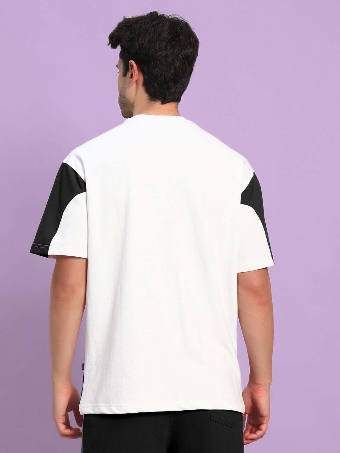 Back view of person wearing CANDOR OVER-SIZED T-SHIRT WHITE BLACK, showcasing the modern streetwear design against a purple background.