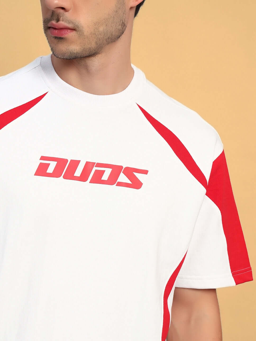 Man wearing CANDOR OVER-SIZED T-SHIRT WHITE RED with red accents and logo, showcasing modern streetwear style on a beige background.
