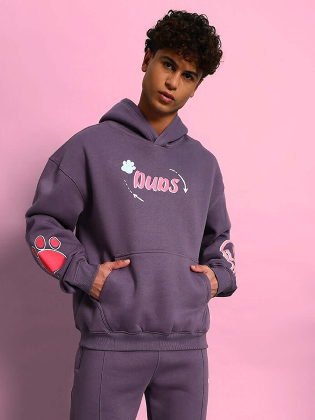 Man wearing CASPER COTTON FLEECE HOODIE VIOLET standing against pink background with hands in pockets.
