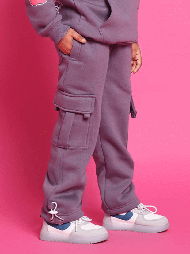 Child wearing violet CASPER co-ord set with pockets, standing against a pink background.