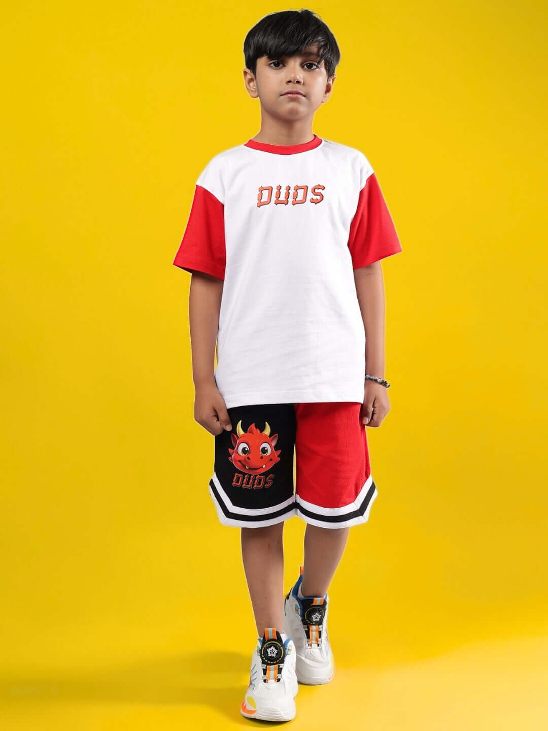 Child wearing CASSIE CO-ORD FOR BOYS & GIRLS WHITE RED, a stylish made-to-order outfit by DUDS, against a yellow background.