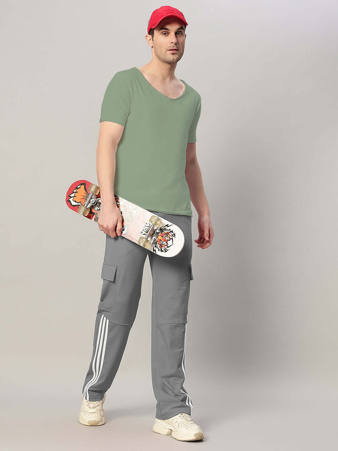Man wearing grey REDROIT 5 Pocket Relaxed Fit Joggers holding skateboard, showcasing casual style with sneakers and red cap.