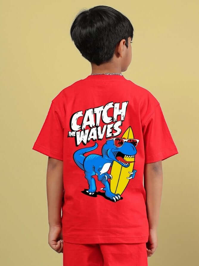 Boy wearing red CATCH THE WAVES T-SHIRT FOR BOYS GIRLS RED with blue dinosaur graphic holding a surfboard, capturing a fun adventure vibe.