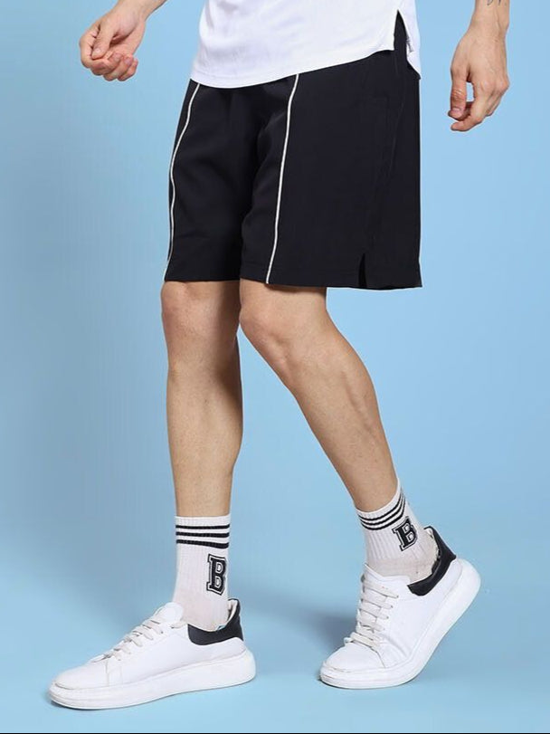 Person wearing CHAMPION ZONE FRONT PLATED SHORTS BLACK with white sneakers on a light blue background
