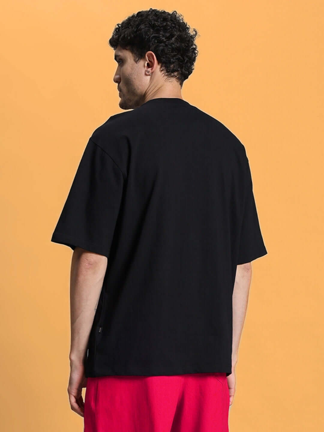 Back view of a person wearing a CHERRY BLOSSOM OVER-SIZED T-SHIRT BLACK with premium heavy gauge fabric on an orange background.