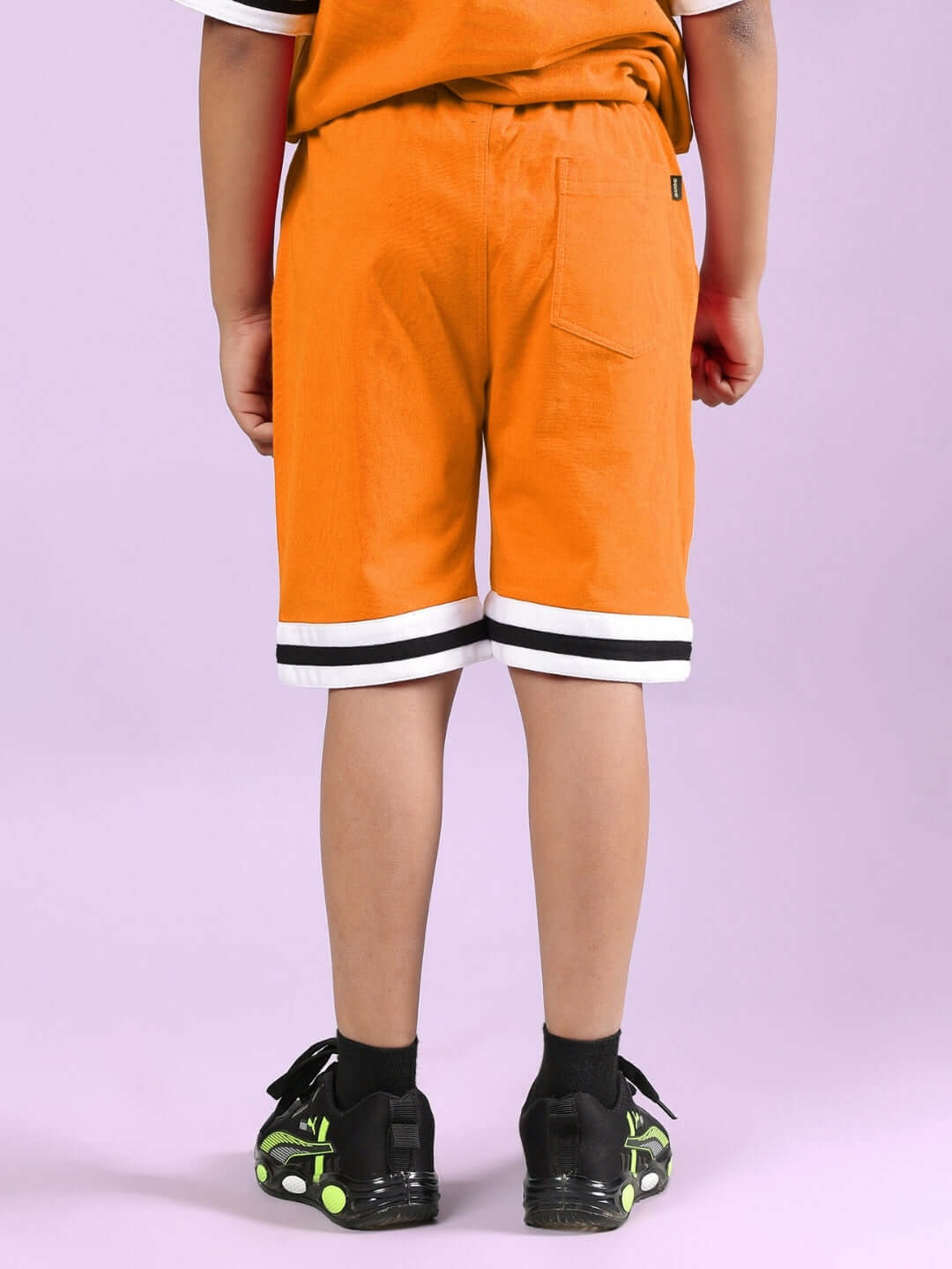 Child wearing CHICAGO PRINTED CO-ORD FOR BOYS & GIRLS ORANGE, featuring orange shorts with white and black trim, rear view, isolated background.