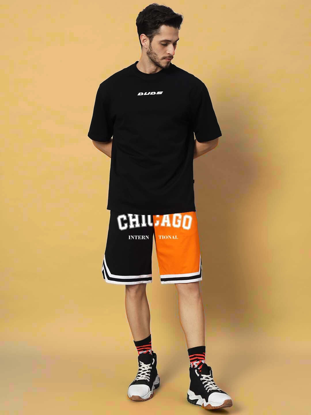 Man wearing Chicago regular fit shorts in orange-black with custom fit option, styled with black top and sneakers.