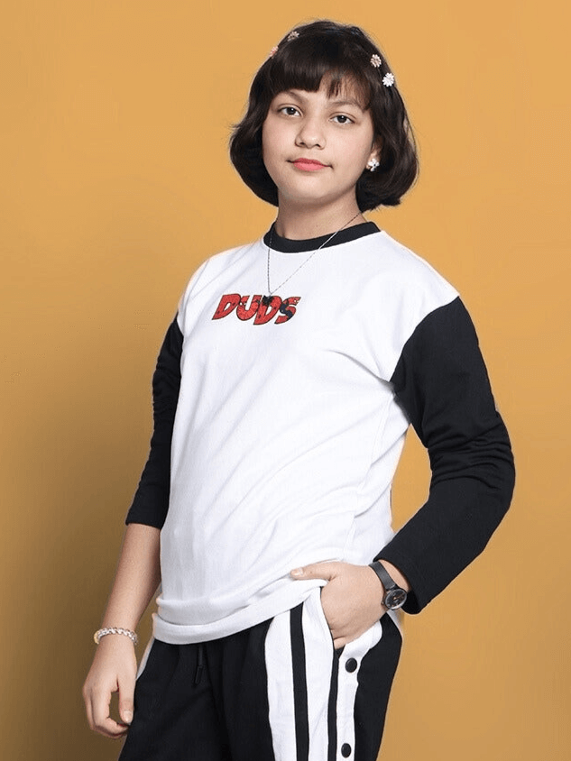 Young person wearing a BITSY oversized sweatshirt by DUDS in white with black sleeves, standing against an orange background.