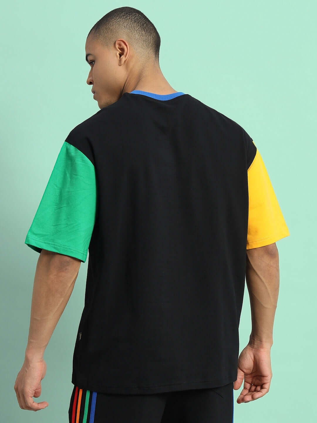 Back view of a model wearing a CHROMA color blocked oversized T-shirt with black base, featuring green and yellow sleeves.