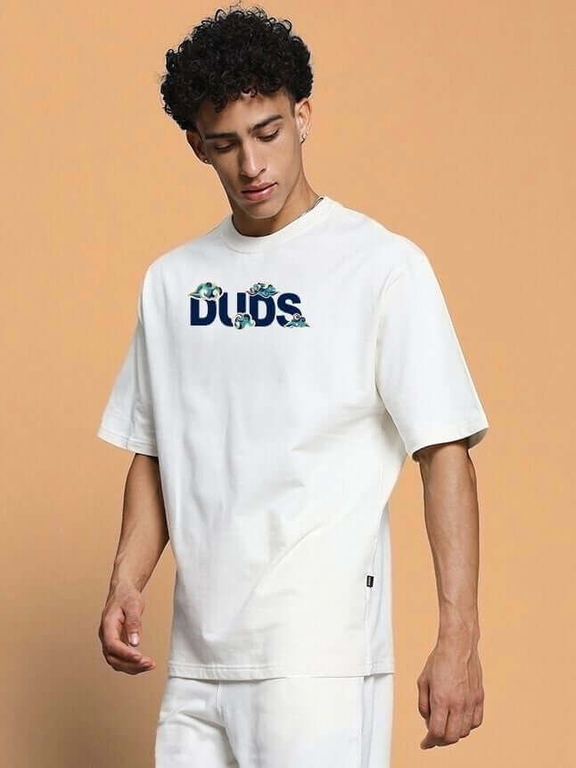Man wearing a CLOUD PRINTED OVERSIZED T-SHIRT OFF WHITE with text design, standing against a beige background.