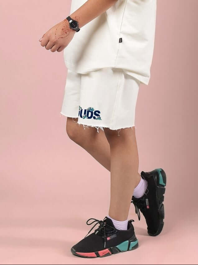 Child wearing CLOUD PRINTED SHORTS FOR BOYS AND GIRLS OFF WHITE with sneakers on a pink background.