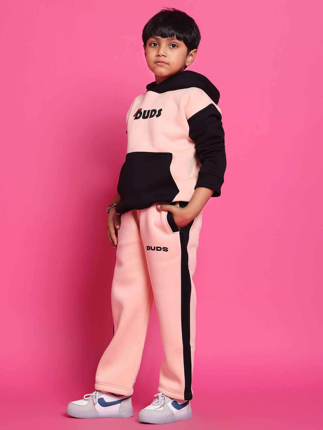 Child wearing Club House fleece jogger in black-beige, standing against pink background, showcasing cozy and stylish kids' fashion.