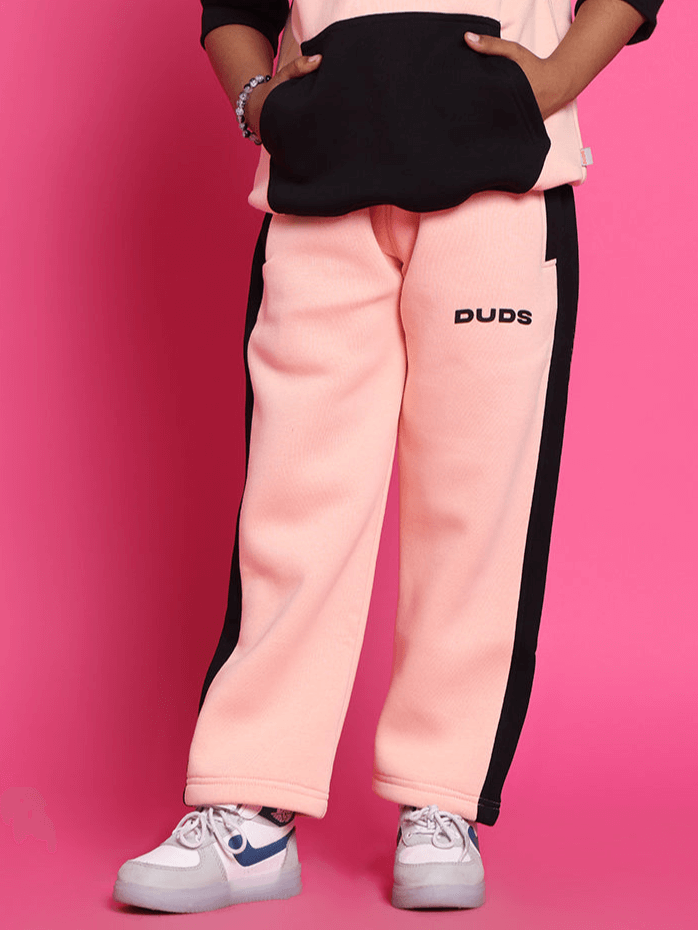 Child wearing black-beige fleece jogger pants with side stripes, standing against a pink background.