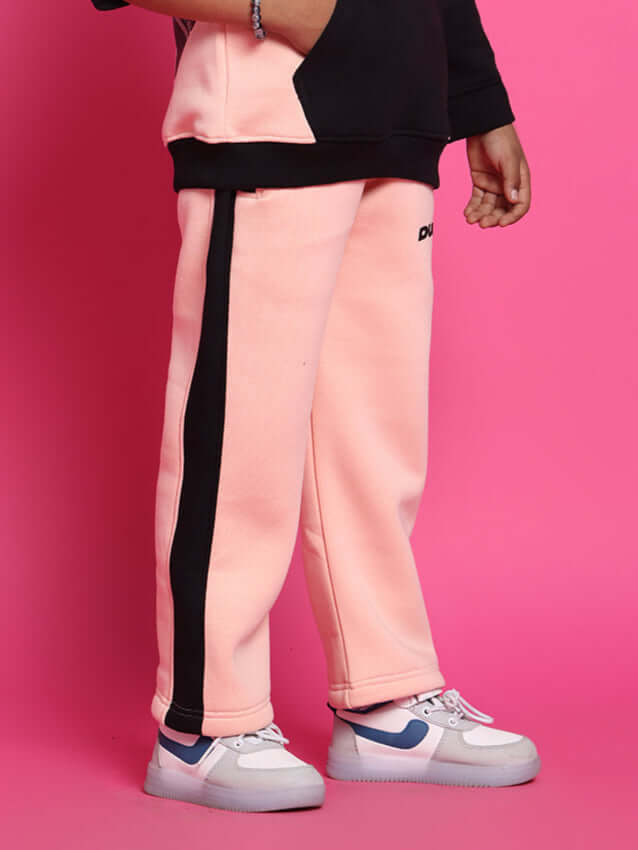Child wearing Club House fleece joggers in black-beige with sneakers against a pink background.