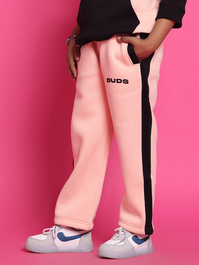 Child wearing Club House fleece jogger in black-beige, showcasing cozy style on vibrant pink background.