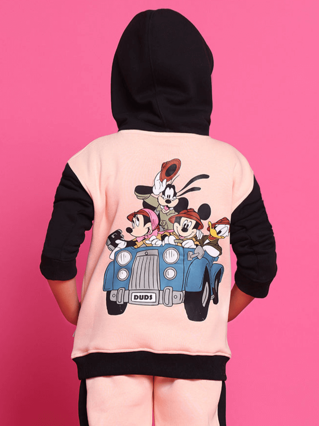 Back view of a child wearing a black and beige oversized hoodie with cartoon characters on a pink background.