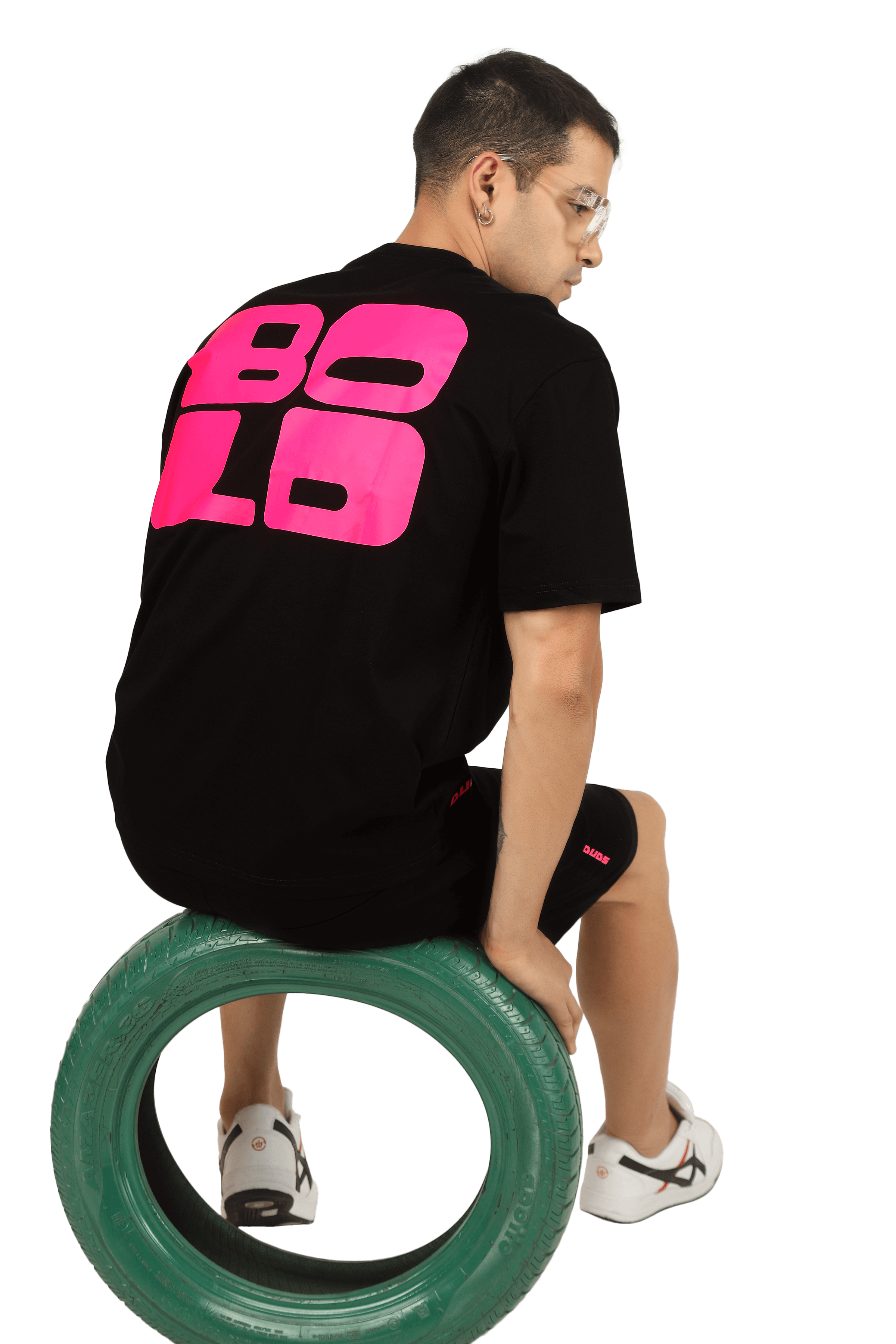 Person wearing a black co-ord set with 'BOLD' print, sitting on a green tire, showcasing trendy casual fashion.