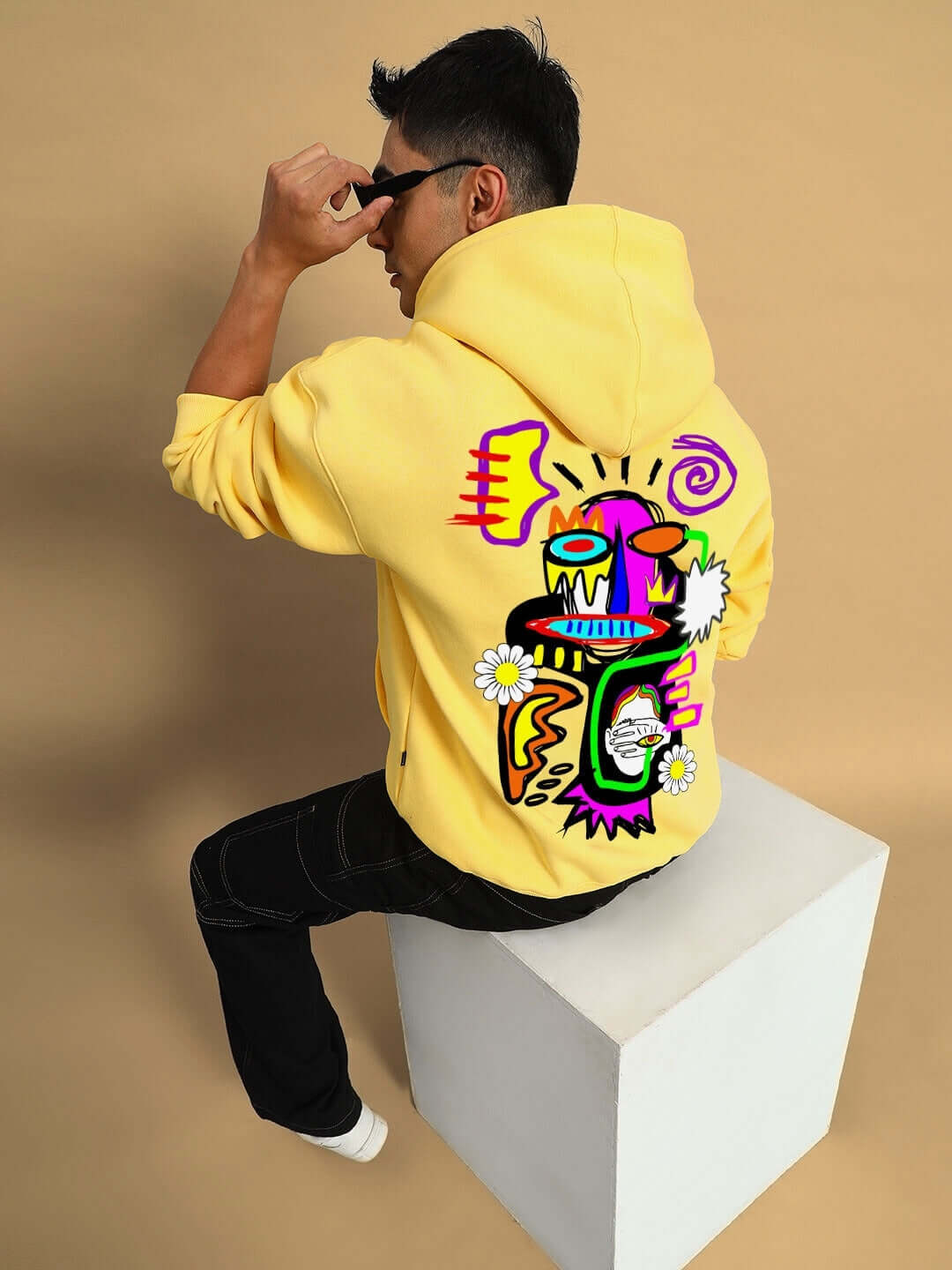 CONFUSED FLEECE OVERSIZED HOODIE YELLOW with colorful graphic design, worn by person sitting on cube, streetwear fashion